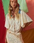 Woman wearing a white lace outfit with colorful accessories against a multicolored background