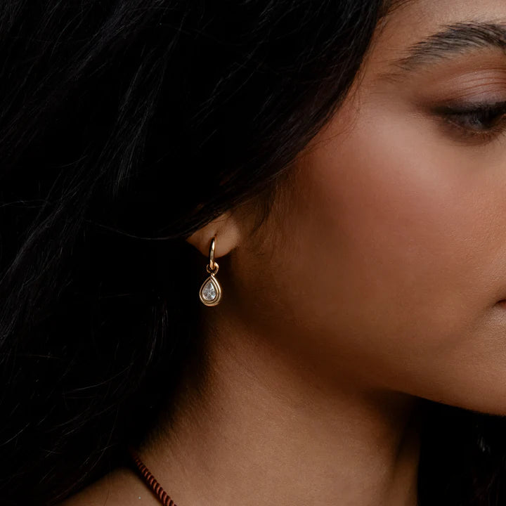 Close-up of a woman wearing a gold earring with a teardrop-shaped gemstone.