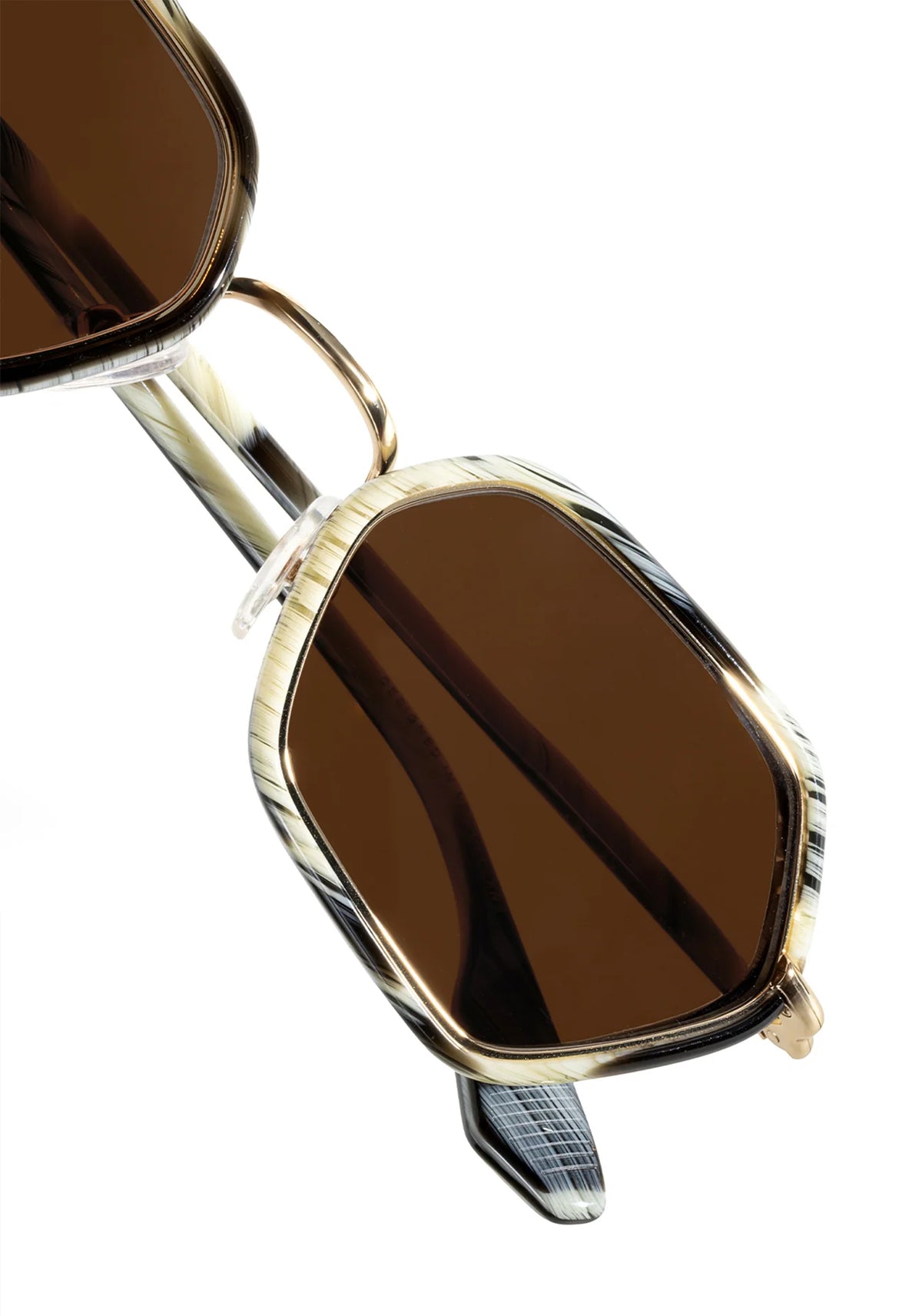 Close-up of a pair of sunglasses with a gold-tone metal frame, dark brown tinted lenses, and a patterned temple arm on a white background.