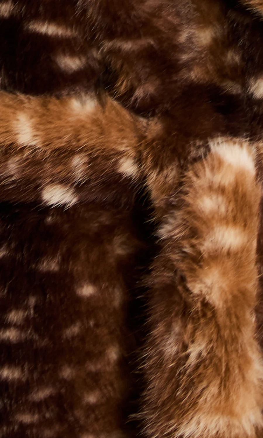 Close-up of a brown faux fur or animal-print textile with dark brown and tan sections and irregular cream spots.