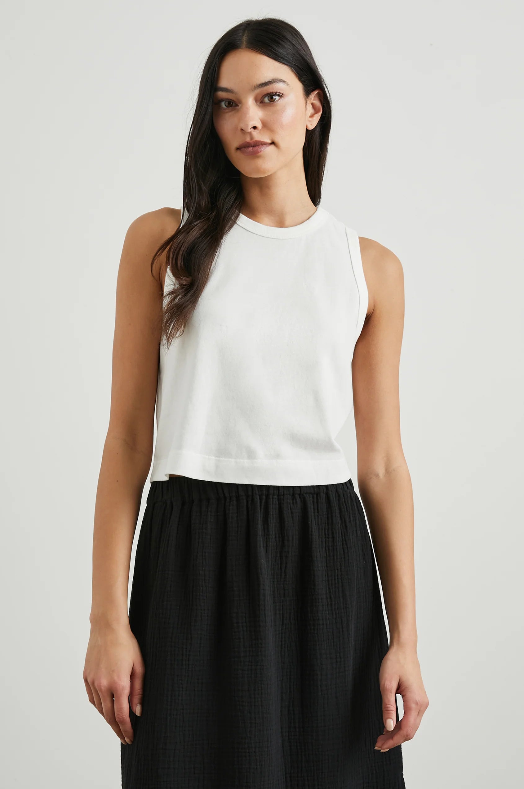 Woman wearing a white sleeveless top and black skirt on a plain background