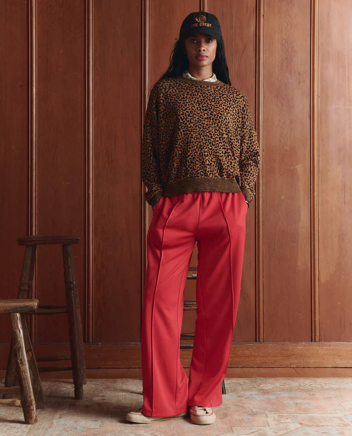 Person wearing a leopard print sweater and red pants standing against a wooden paneled wall.