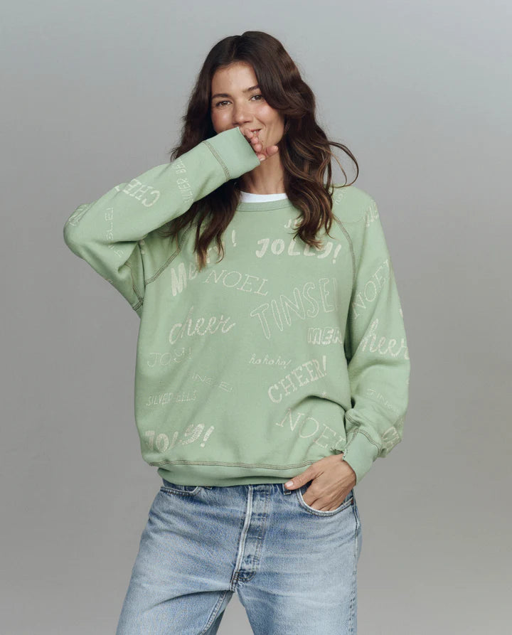 Woman wearing a light green sweatshirt with text and blue jeans on a gray background