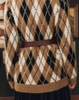 A close-up of a person wearing a fuzzy knit sweater with a brown, cream, and black argyle pattern, styled with a brown belt, shown from the back.