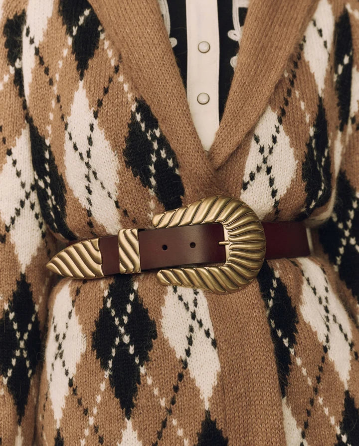 A close-up of a brown leather belt with a large, ornate gold-toned buckle, worn over a tan, black, and white argyle knit cardigan.