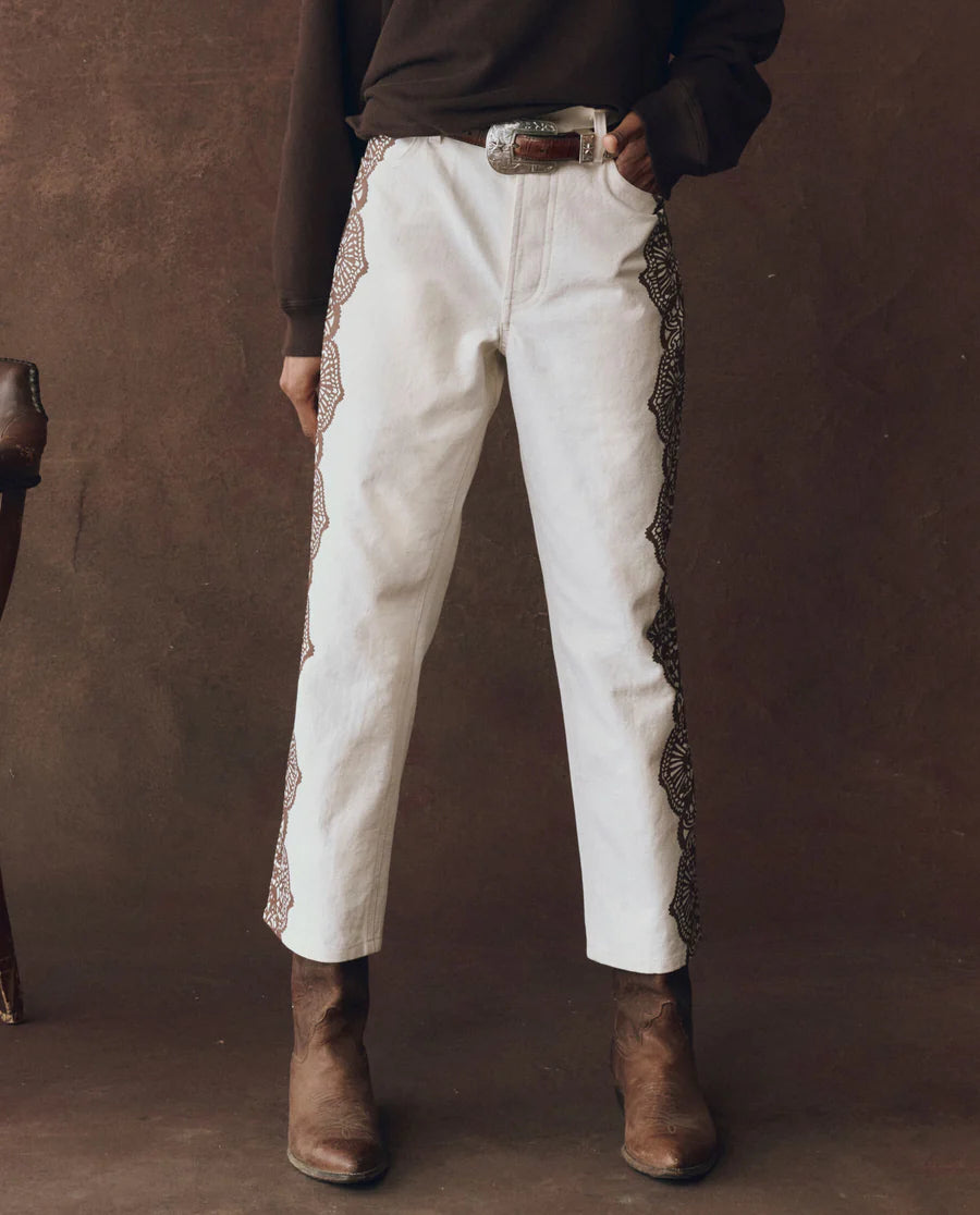Person wearing wayne jeans with decorative trim and brown boots against a brown background, front