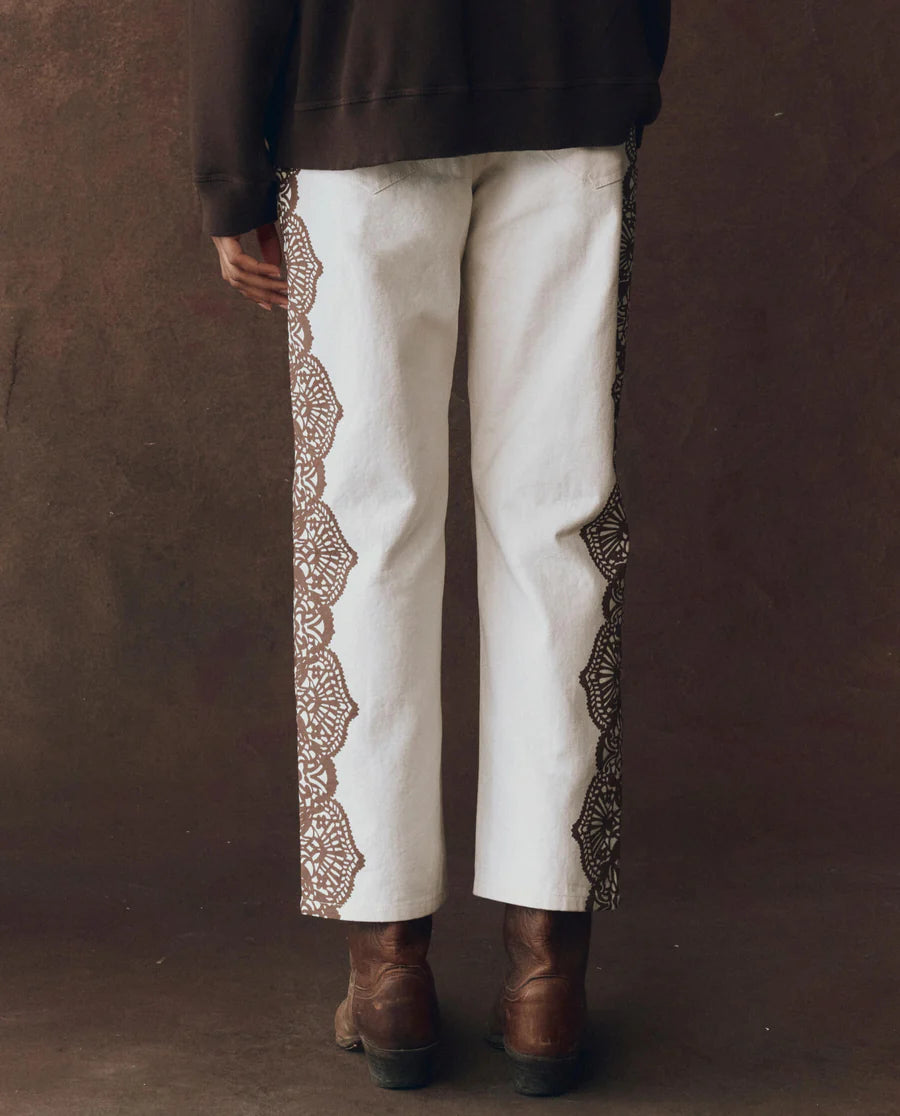 Person wearing wayne jeans with decorative trim and brown boots against a brown background, back