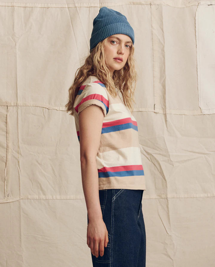 Person wearing a striped shirt and blue beanie against a textured beige background