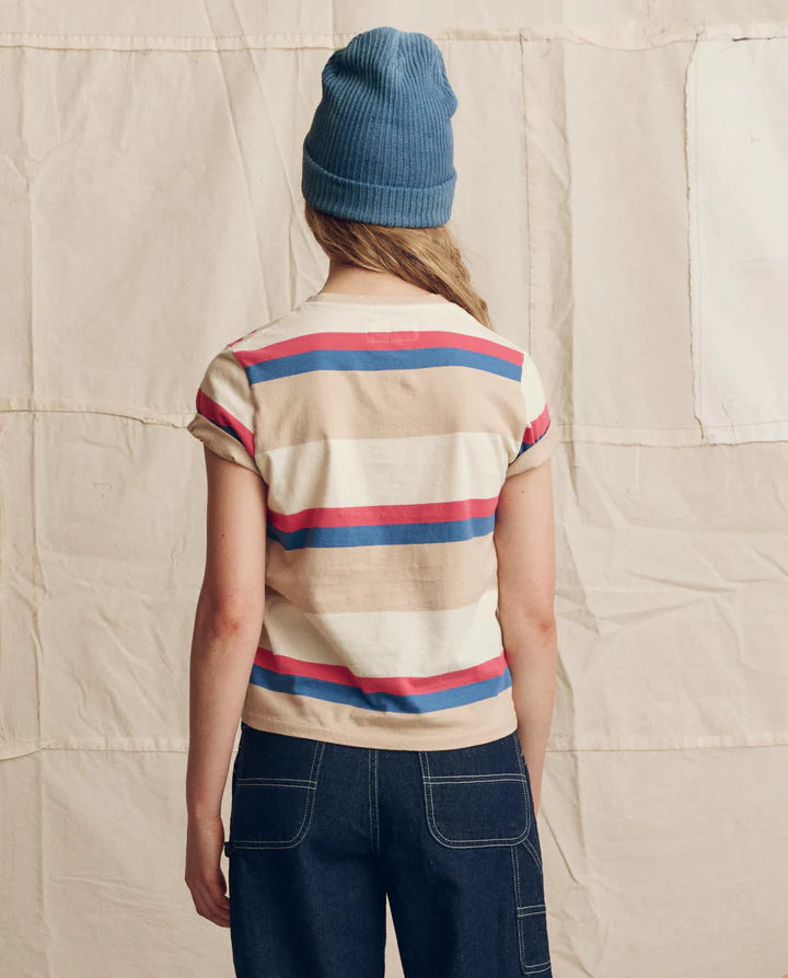 Person wearing a striped shirt and blue beanie standing against a textured beige wall.