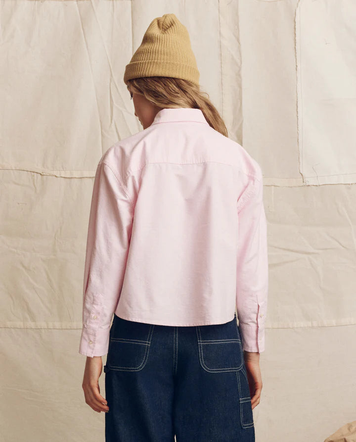 Person wearing a pink shirt and beige beanie standing against a textured beige wall.