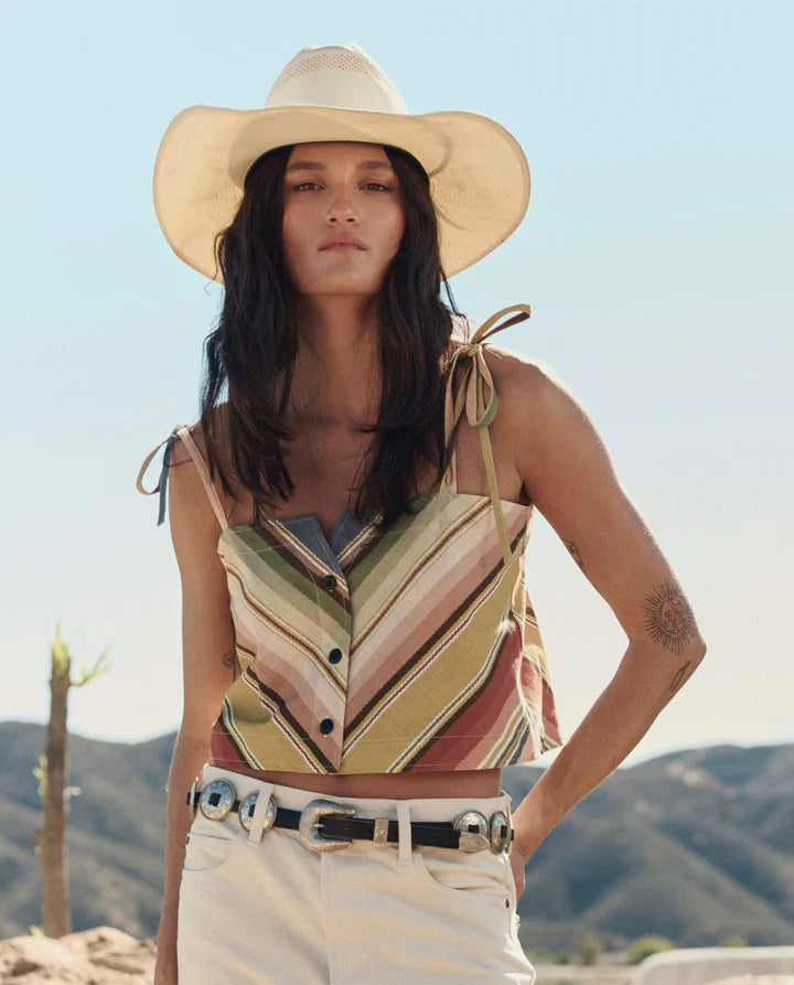 Woman wearing a colorful striped top and wide-brimmed hat with a desert landscape in the background