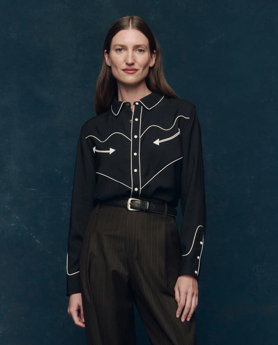 Woman wearing the western shirt black blouse with white embroidery against a dark blue background