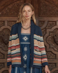 Woman wearing a colorful striped cardigan over a patterned dress against a wooden background