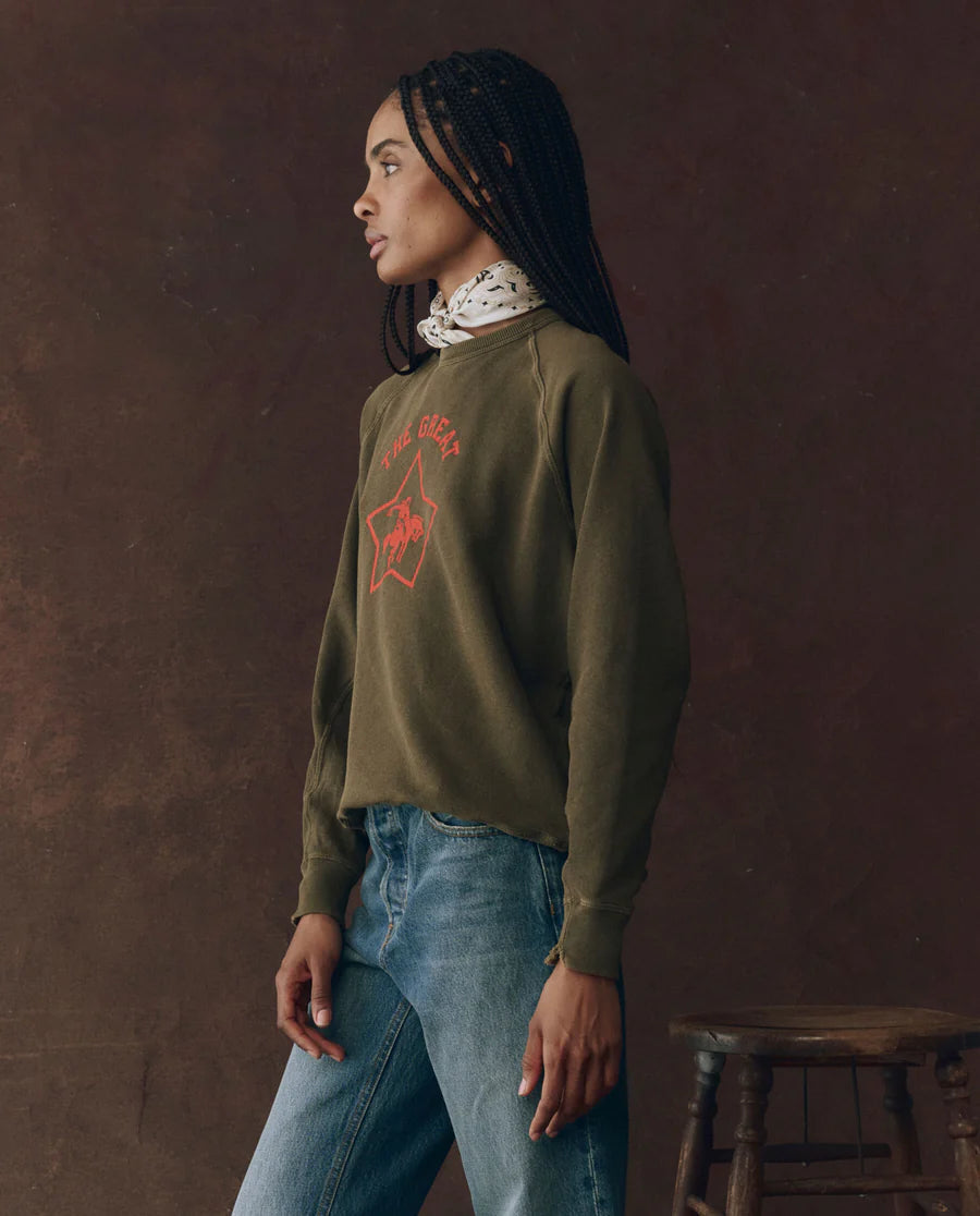 The college sweatshirt rodeo star army green on a model wearing jeans with a brown background, side view