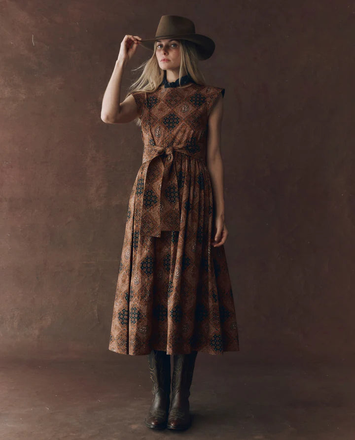 Woman wearing a patterned dress and hat against a brown background