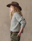 grey cardigan on a model with green pants and a western hat on a cream background, side