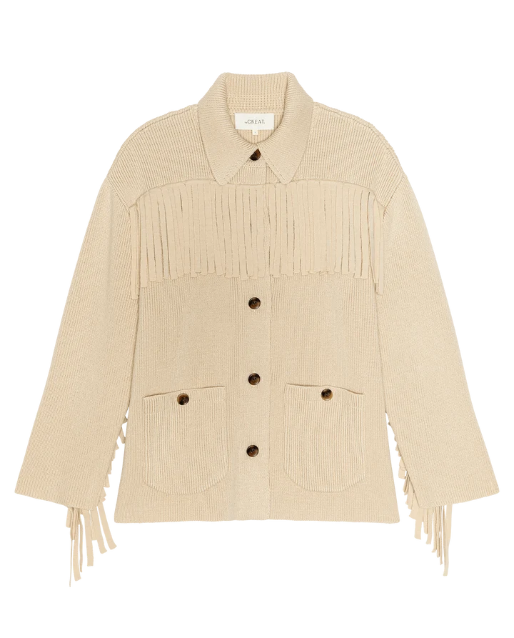 A cream-colored ribbed knit cardigan featuring fringe detailing across the chest and cuffs, a pointed collar, and front button closure with two patch pockets.