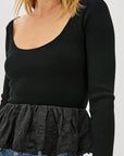 Black long-sleeve top with a ruffled bottom worn by a person on a white background detail view