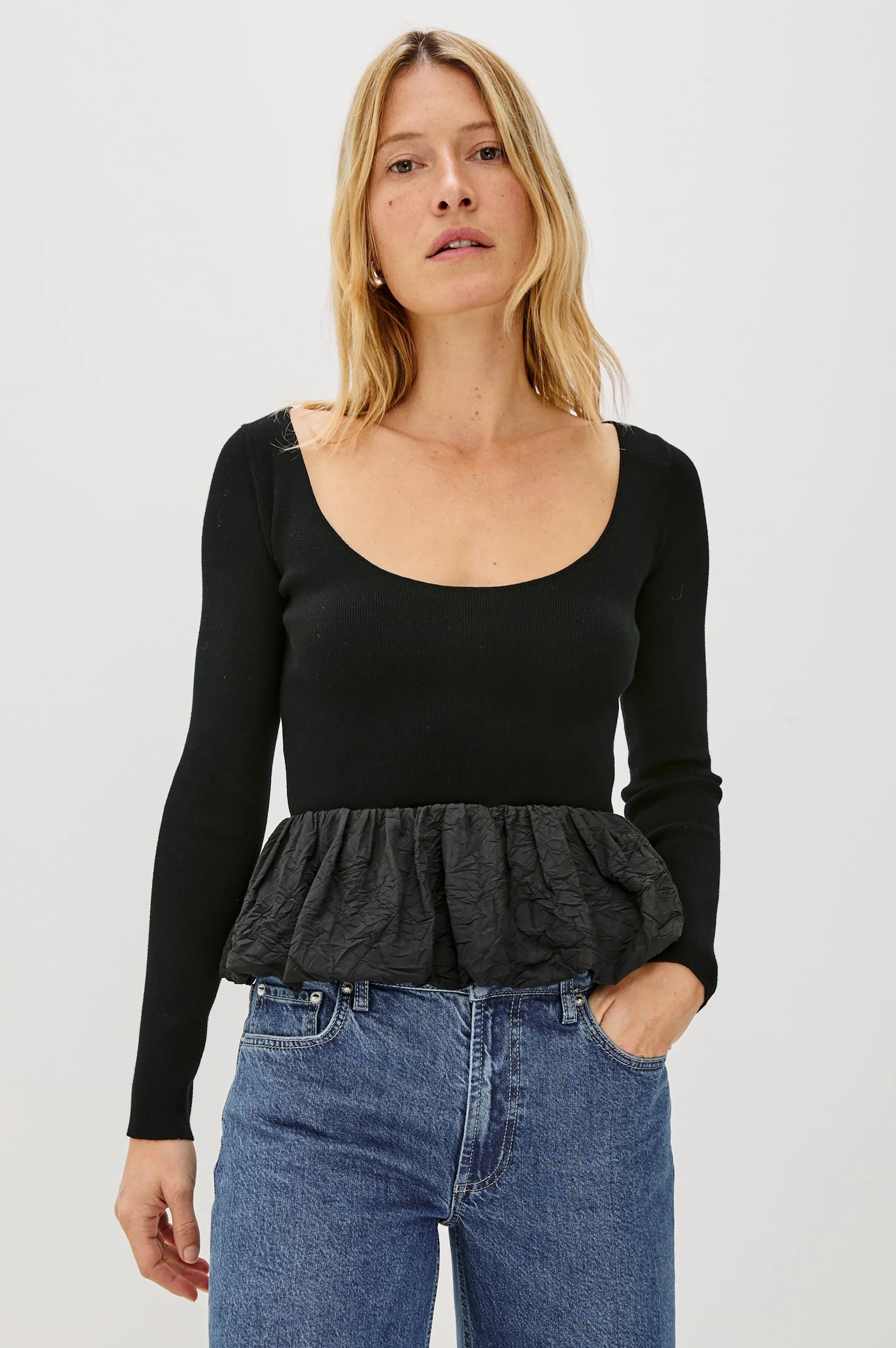 Woman wearing a black long-sleeve top with a peplum waist and blue jeans on a white background front view