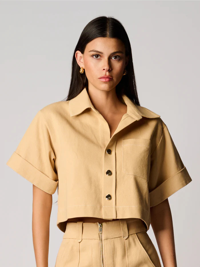 Woman wearing a beige short-sleeve shirt with buttons on a plain background
