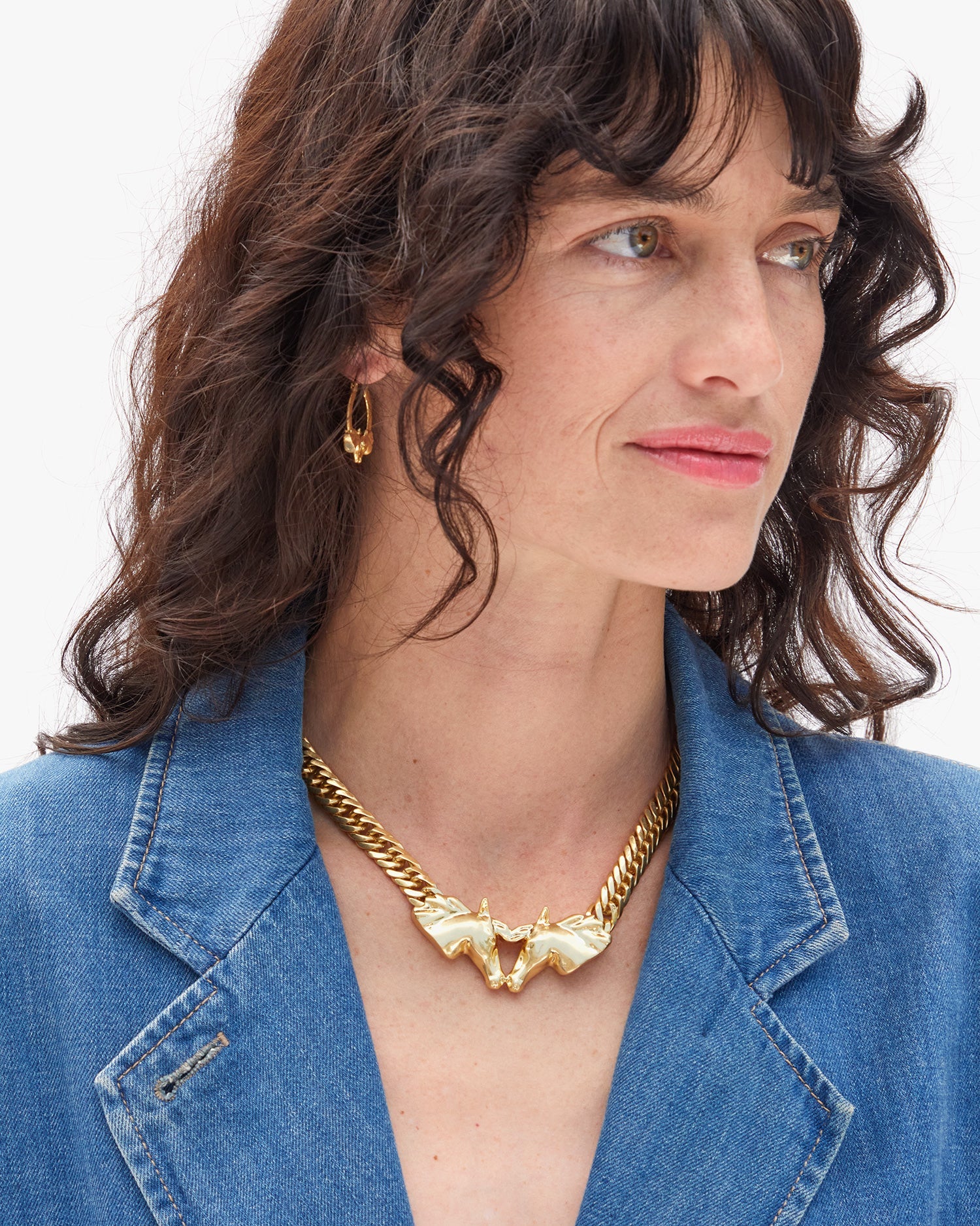 Woman wearing a gold necklace and earrings with a blue denim jacket on a white background