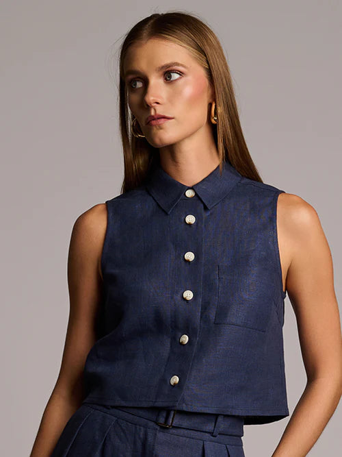 Woman wearing a navy sleeveless button-up top against a gray background