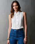 Woman wearing a white sleeveless blouse and blue jeans against a gray background