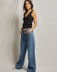 Woman wearing a black tank top and blue jeans against a plain background, full body