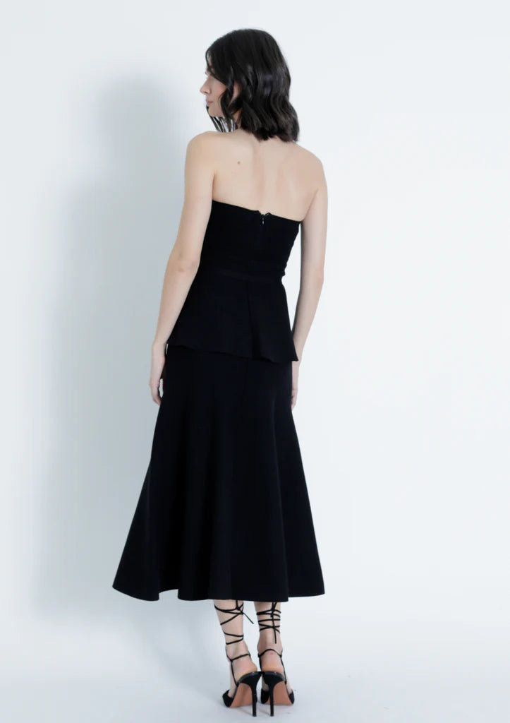 Woman wearing a black strapless dress with a white background back view