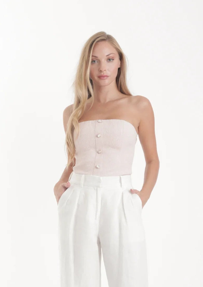 Woman wearing a strapless top and white pants on a white background