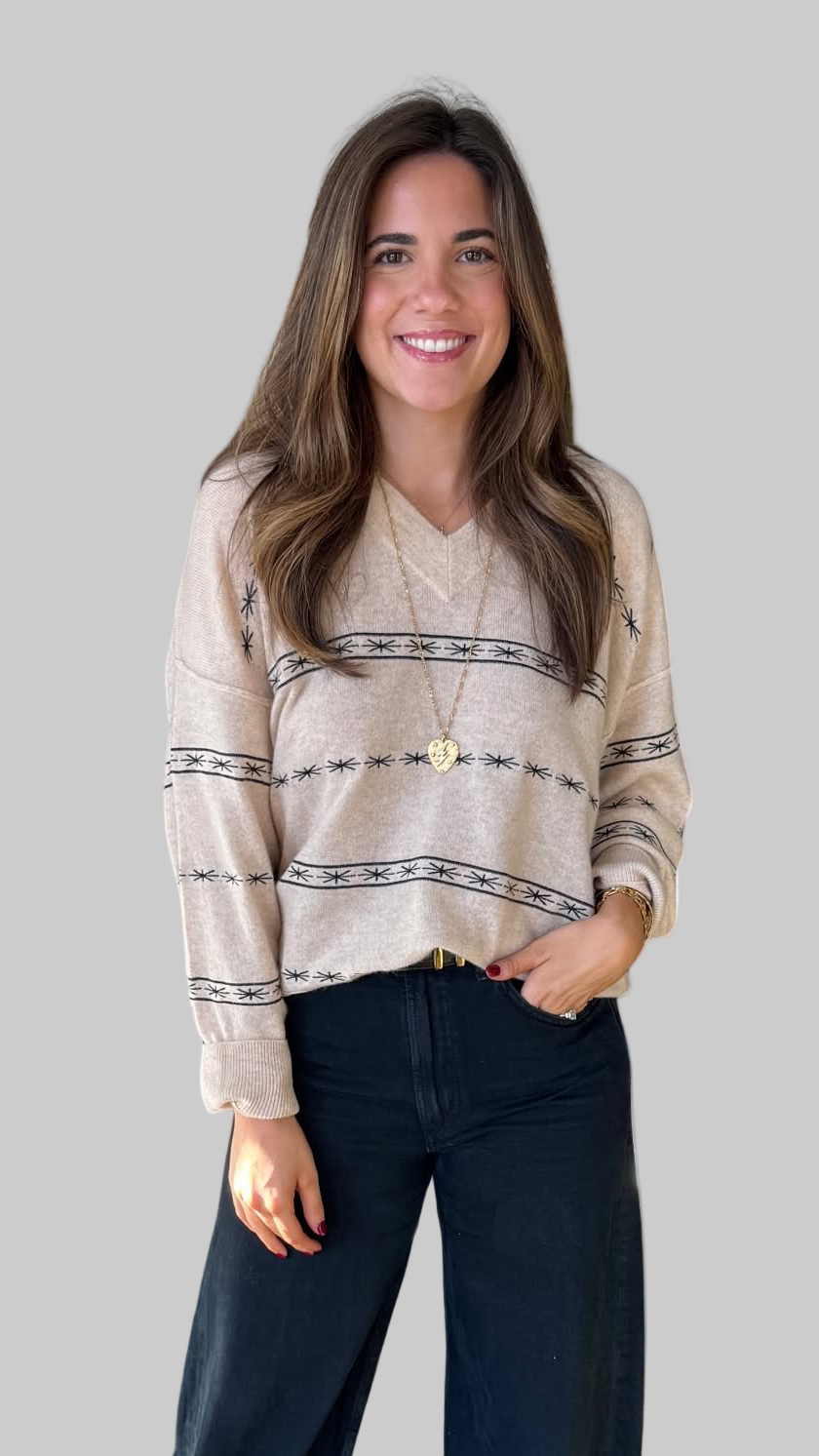 Woman wearing a beige patterned sweater and dark pants on a light background