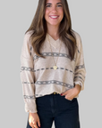 Woman wearing a beige patterned sweater and dark pants on a light background
