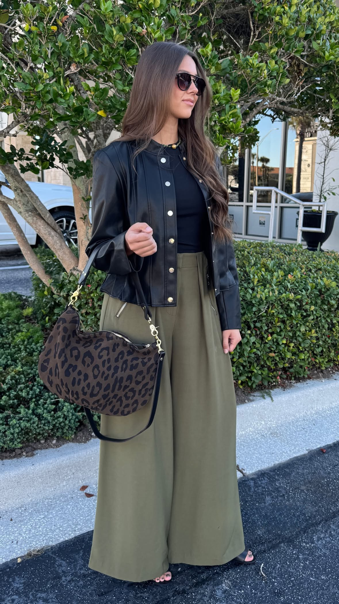 Woman in black jacket and green pants with leopard print bag outdoors