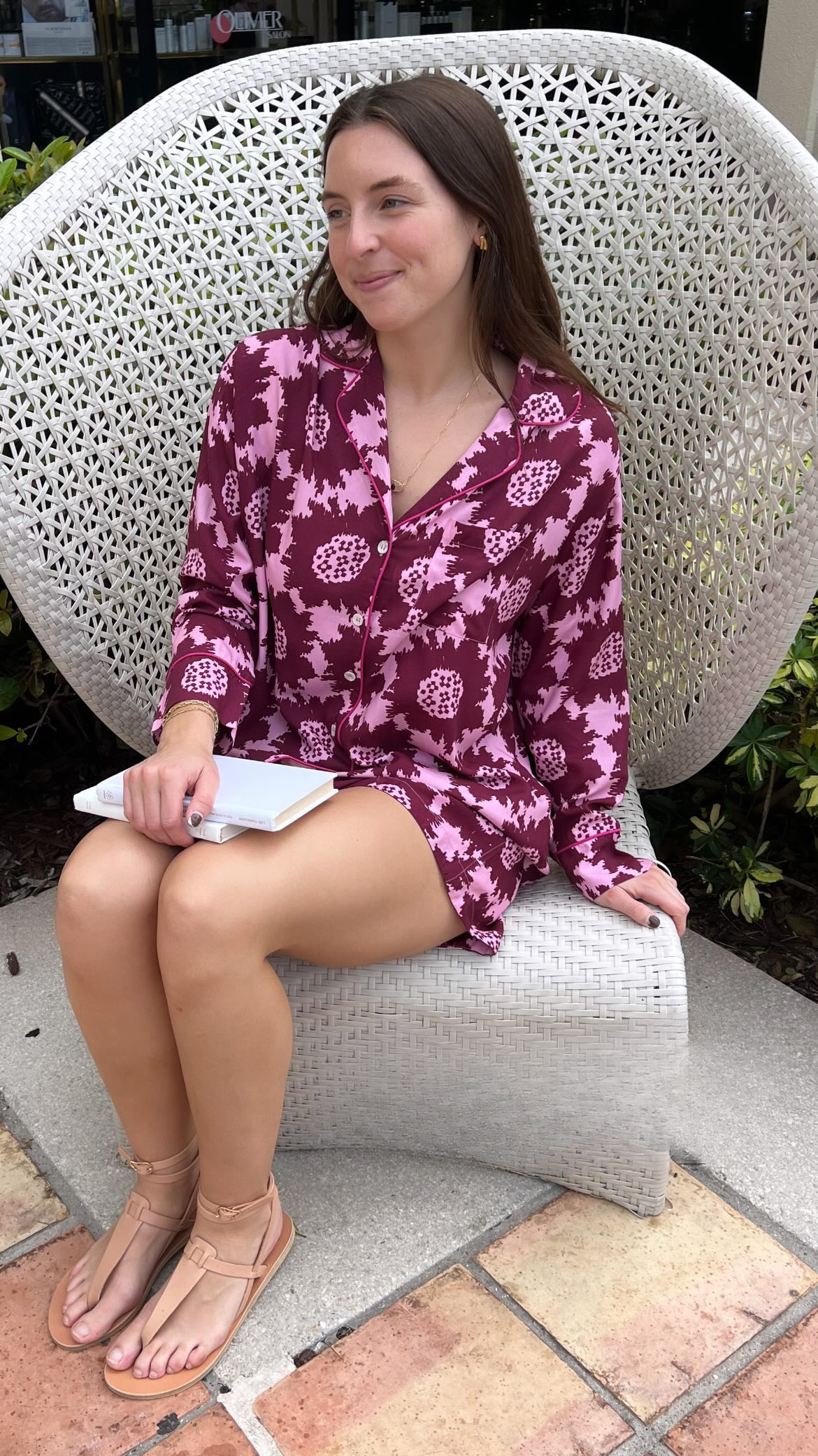 Woman in a pink and purple patterned pj set sitting on a white chair outdoors.
