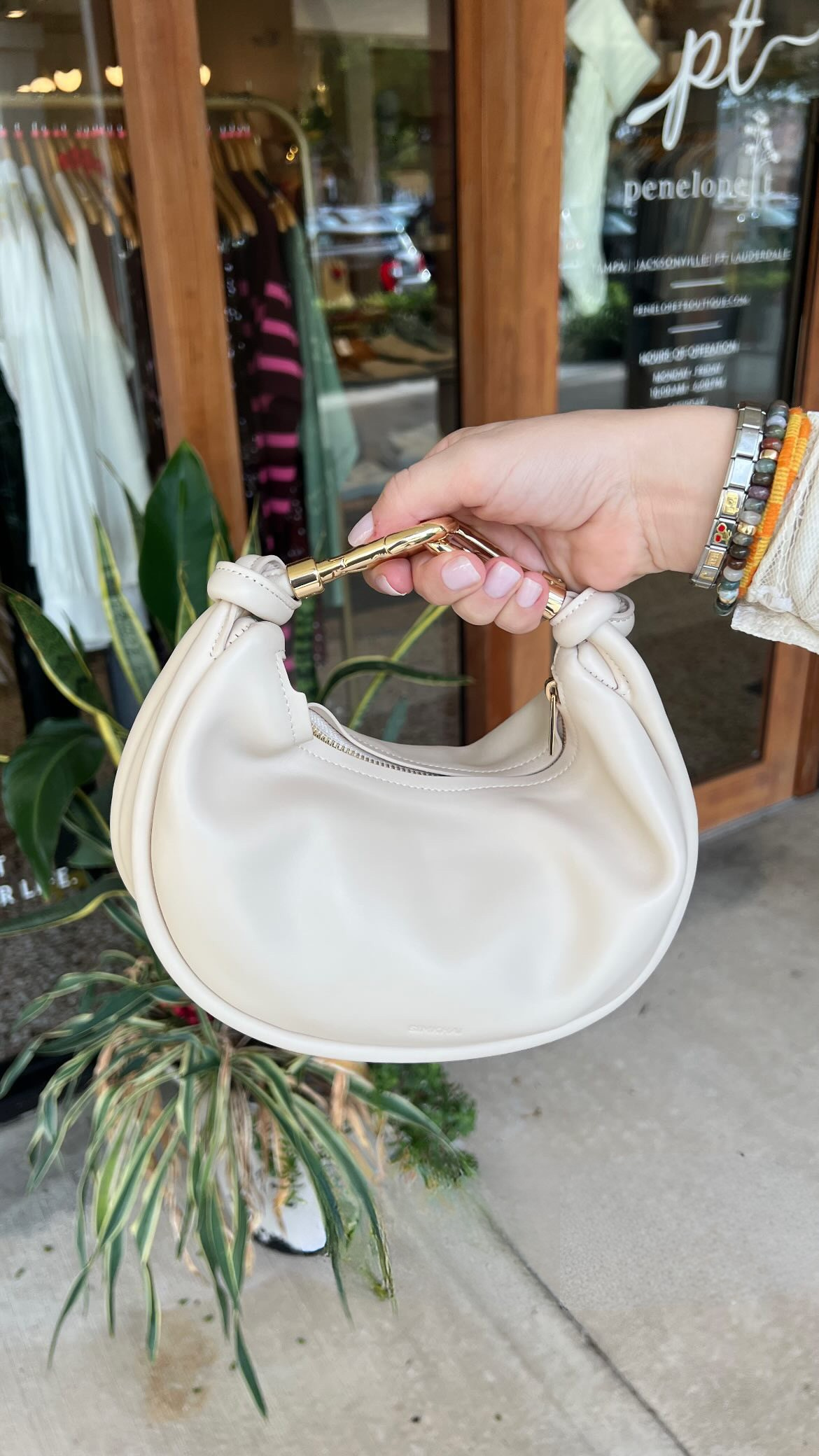 Hand holding a white handbag with gold handle in front of a store entrance