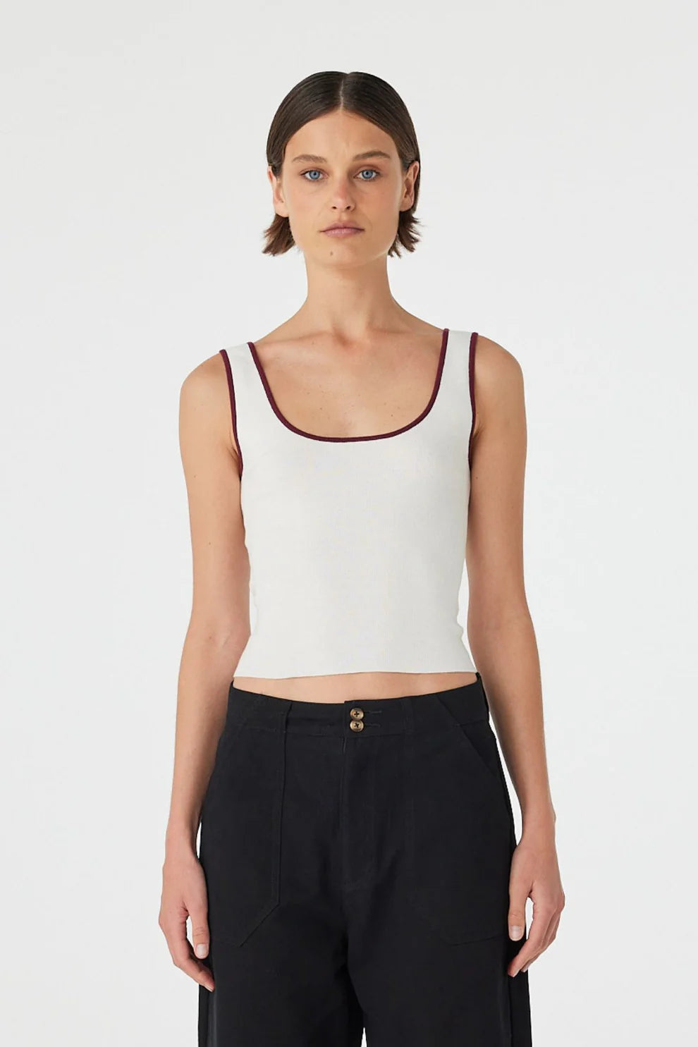 Woman wearing a white tank top with a brown trim on a plain background