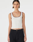 Woman wearing a white tank top with a brown trim on a plain background
