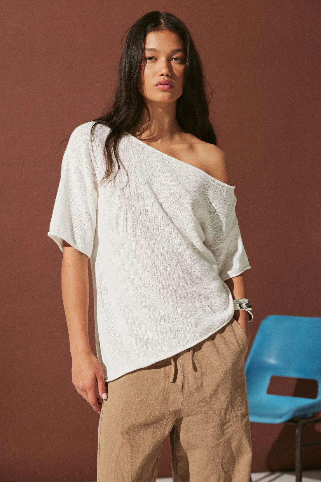Woman wearing a white off-shoulder top and brown pants against a brown background