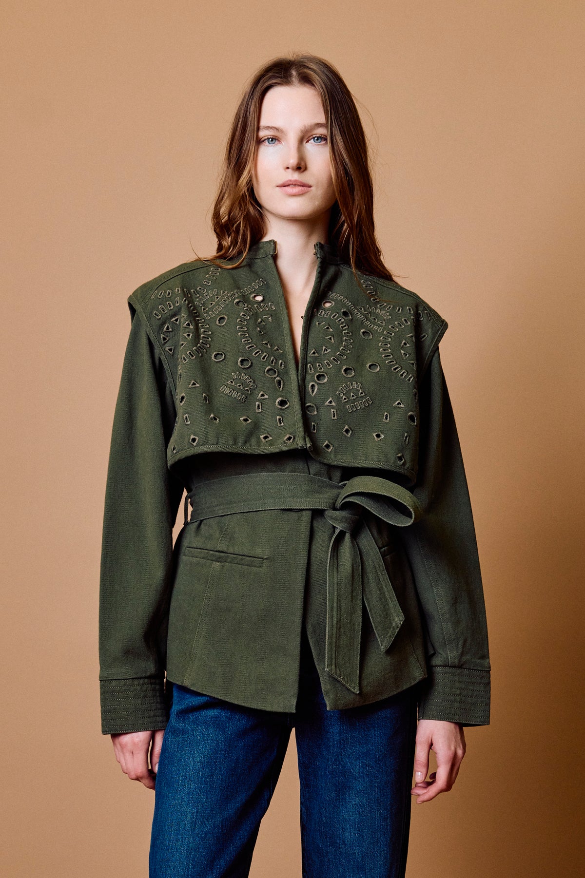 Woman wearing a green jacket with intricate detailing on a brown background
