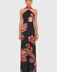 A model wearing a black halter-neck maxi dress with a red, orange, and white paisley and floral pattern, paired with a matching red neck scarf, against a light gray background.
