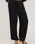 Black wide-leg drawstring pants shown on a model from the waist down, paired with black strappy high-heeled sandals against a light gray studio background.