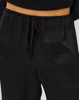 Close-up of a person wearing black drawstring sweatpants and a black ribbed cropped top, showing the waistband and fabric texture against a light neutral background.