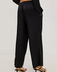 Black wide-leg trousers shown from the back on a model, paired with black strappy high-heeled sandals against a plain white studio background.