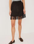 model wearing a fringe plaid skirt with a grey top, loafers, on a light grey background 