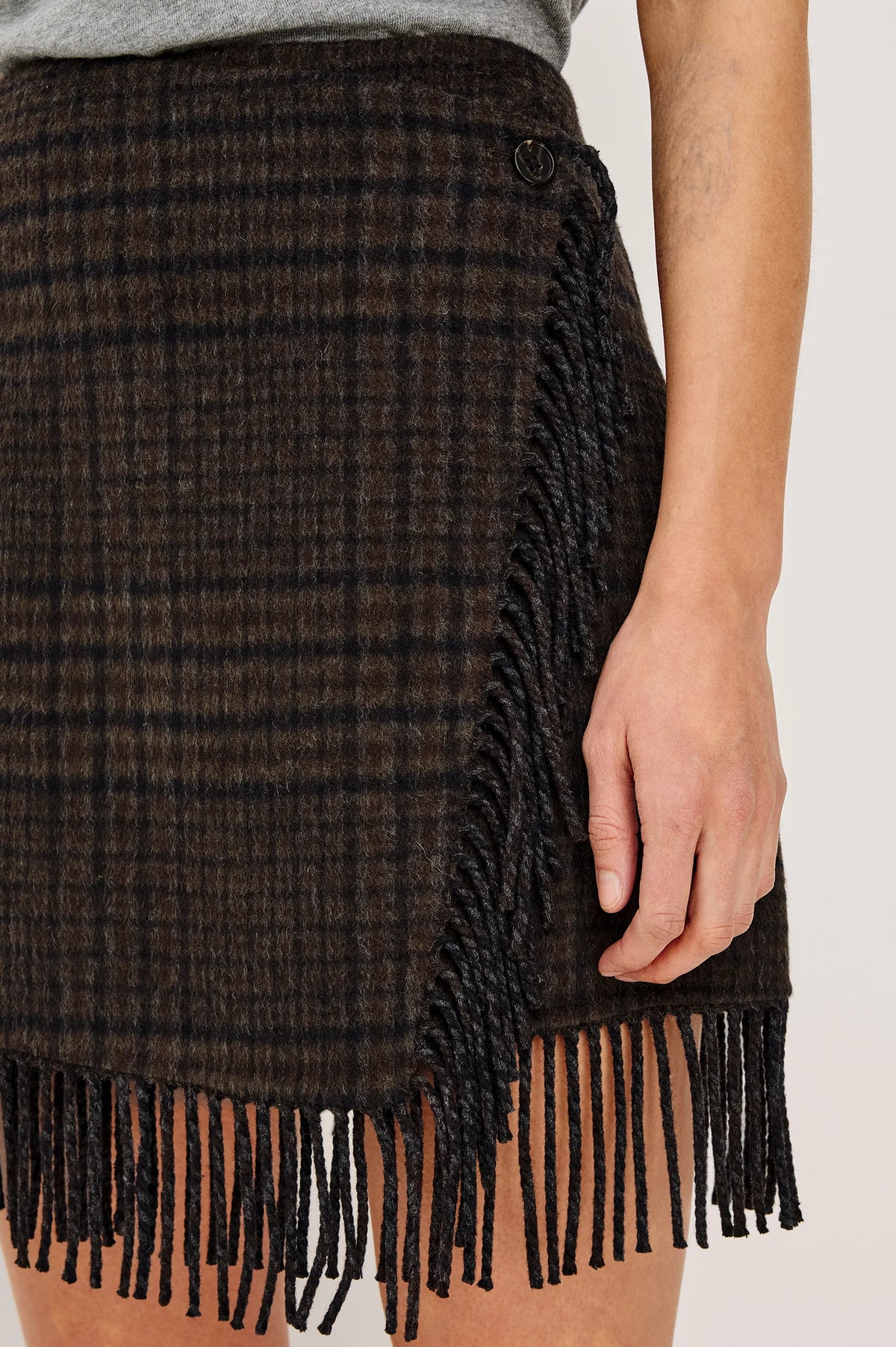 model wearing a fringe plaid skirt with a grey top, loafers, on a light grey background 
