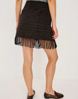 model wearing a fringe plaid skirt with a grey top, loafers, on a light grey background 