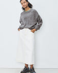 Person wearing a gray sweater and white skirt with black shoes on a white background