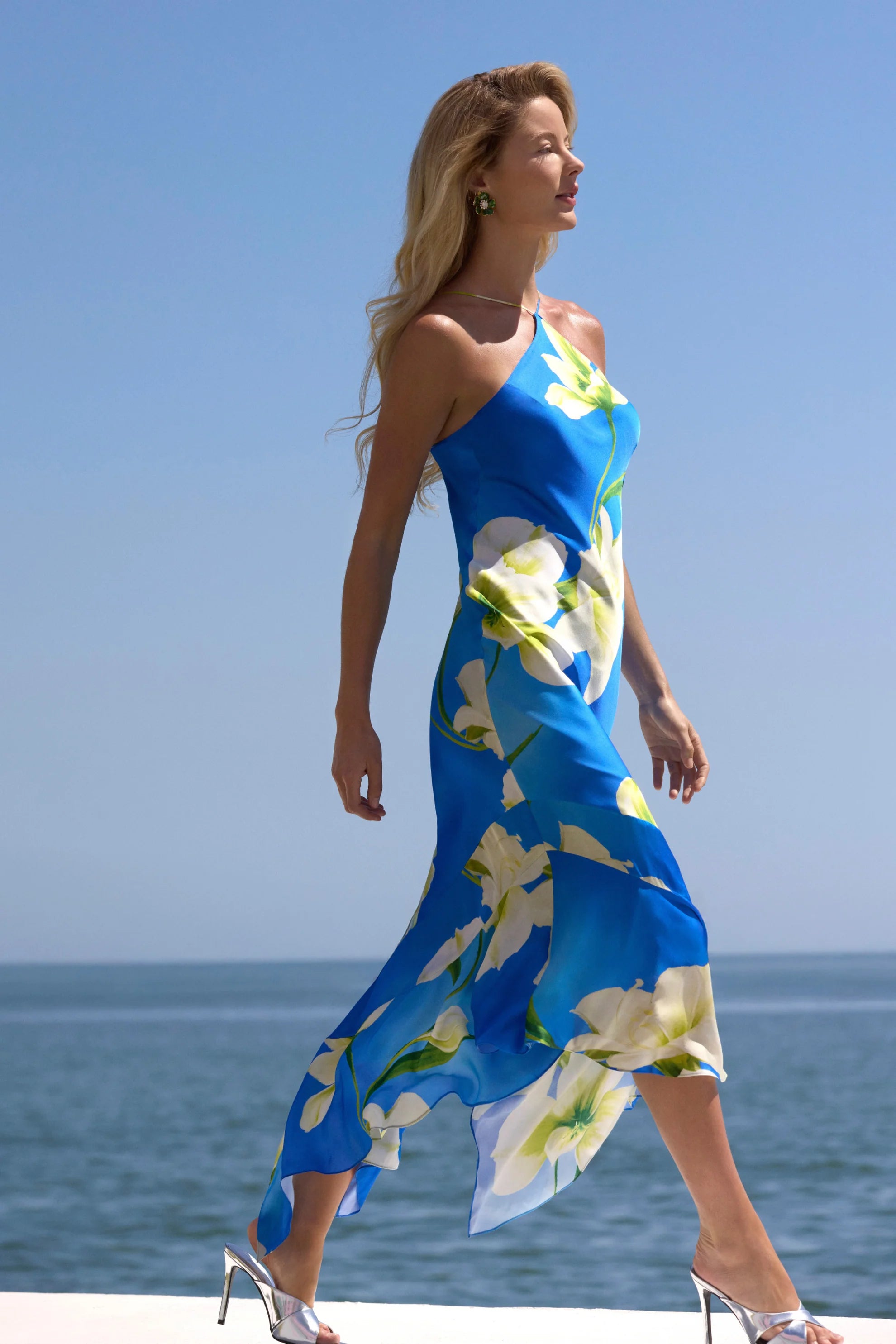 model wearing a blue dress with white flowers walking near the ocean