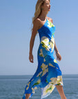 model wearing a blue dress with white flowers walking near the ocean