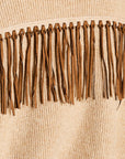 Close-up of a beige ribbed knit garment with a horizontal band of medium brown fringe trim across the chest.